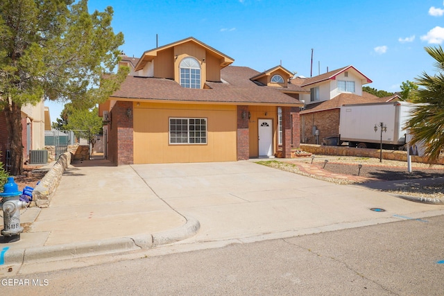 traditional-style house featuring central AC unit, a gate, concrete driveway, fence, and brick siding