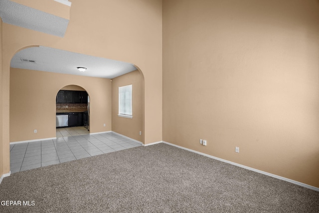carpeted empty room with arched walkways, tile patterned flooring, visible vents, and baseboards