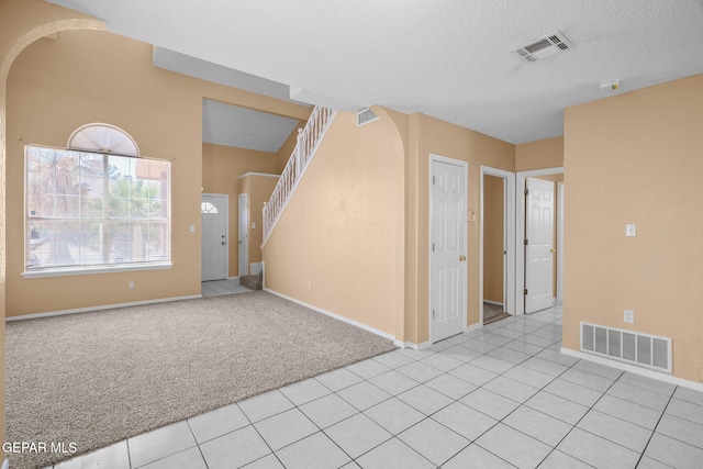 unfurnished living room featuring arched walkways, visible vents, and light carpet