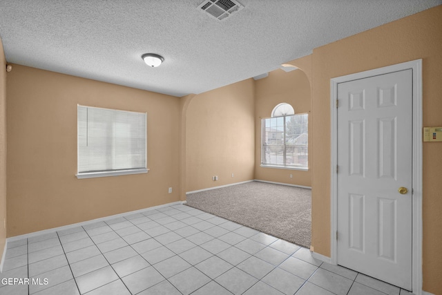 empty room with a textured ceiling, light tile patterned flooring, arched walkways, light colored carpet, and visible vents
