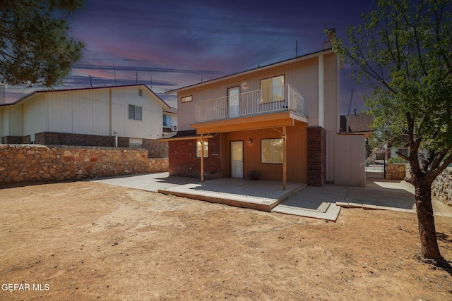 back of house at dusk with brick siding, a patio area, a balcony, and fence