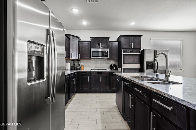 kitchen with tasteful backsplash, a sink, appliances with stainless steel finishes, light stone countertops, and recessed lighting