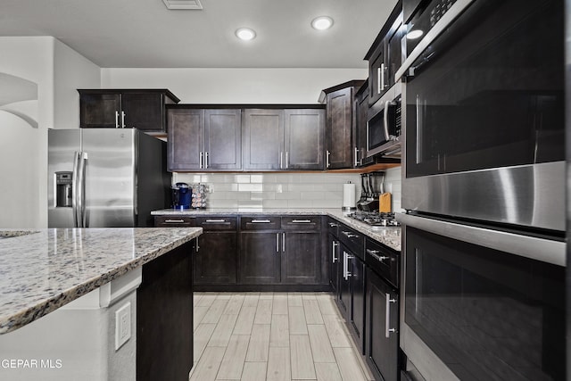 kitchen with tasteful backsplash, appliances with stainless steel finishes, arched walkways, light stone countertops, and recessed lighting