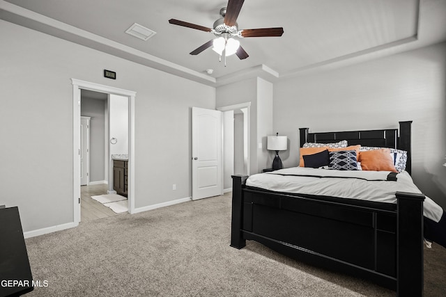 bedroom with a raised ceiling, connected bathroom, baseboards, and light carpet