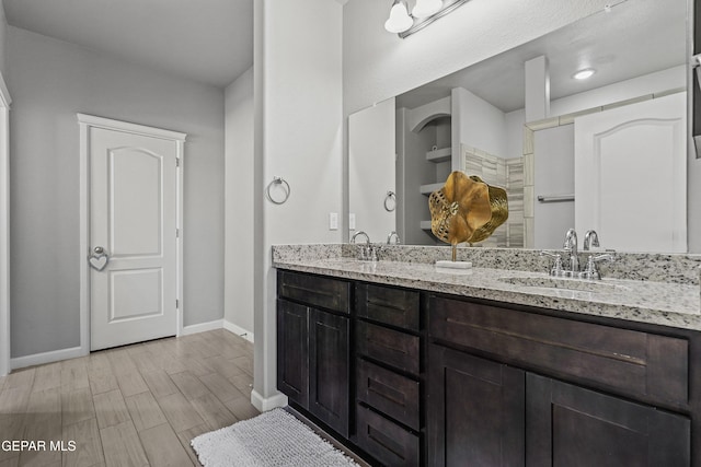 full bath featuring double vanity, a sink, wood finished floors, and baseboards