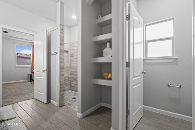 interior space with built in features, tiled shower, wood finished floors, and baseboards