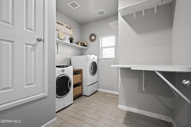 clothes washing area with washing machine and dryer, visible vents, baseboards, light wood finished floors, and laundry area
