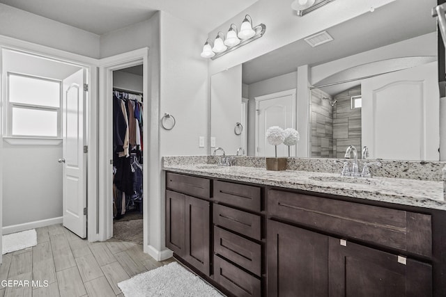 full bathroom with double vanity, a sink, a spacious closet, and baseboards