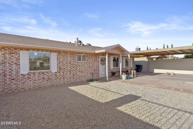 view of front facade featuring fence, a patio area, brick siding, and roof with shingles