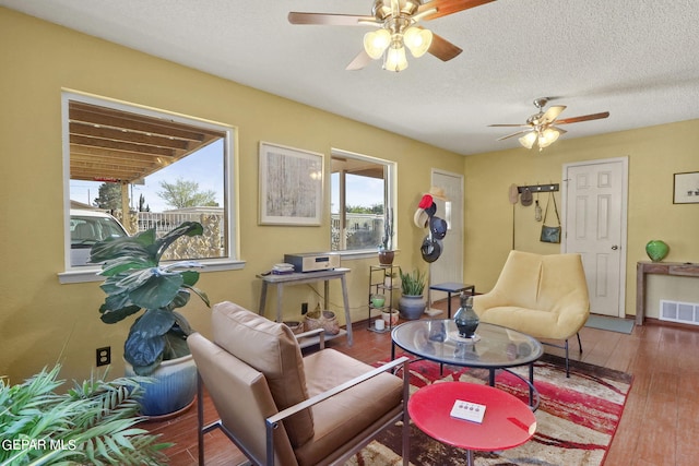 living area with a textured ceiling, wood finished floors, visible vents, and a ceiling fan