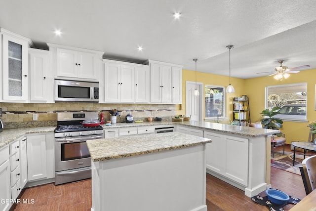 kitchen with decorative backsplash, stainless steel appliances, white cabinets, a peninsula, and dark wood-type flooring