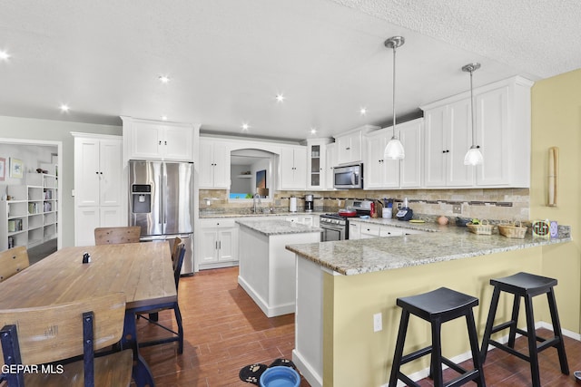 kitchen featuring stainless steel appliances, a peninsula, decorative backsplash, and dark wood finished floors
