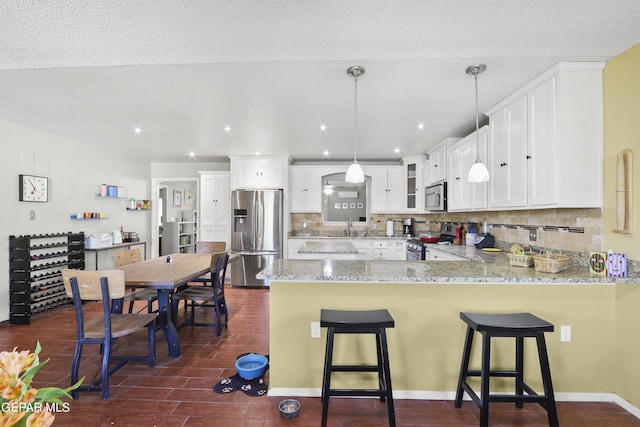 kitchen featuring a peninsula, a sink, backsplash, light stone counters, and appliances with stainless steel finishes