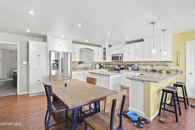 kitchen with stainless steel appliances, wood finished floors, backsplash, and white cabinetry