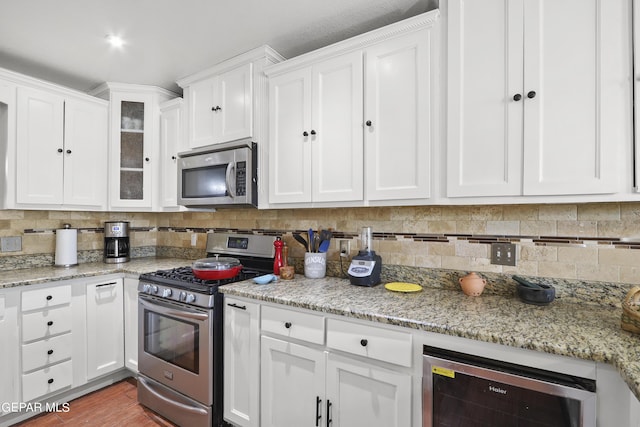 kitchen with white cabinets, backsplash, appliances with stainless steel finishes, light stone countertops, and wine cooler