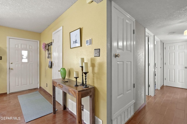 entrance foyer featuring a textured wall, baseboards, wood finished floors, and a textured ceiling