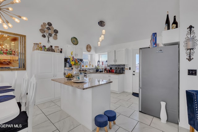 kitchen with white cabinets, a center island, freestanding refrigerator, a notable chandelier, and light stone counters
