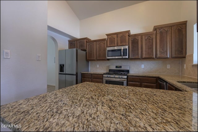 kitchen with appliances with stainless steel finishes, stone counters, tasteful backsplash, and arched walkways