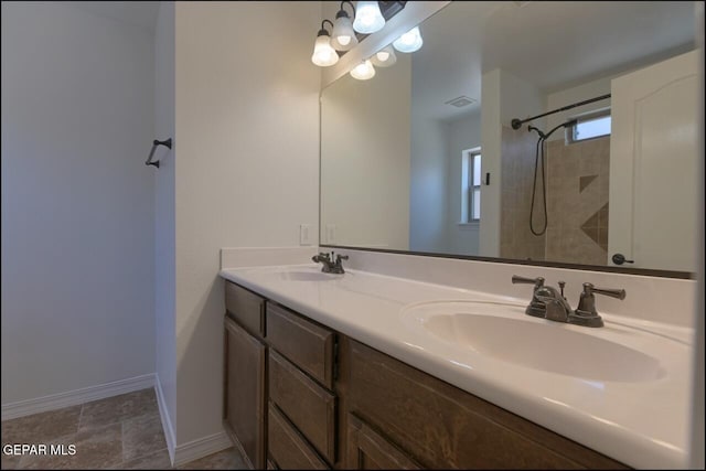 bathroom with a tile shower, double vanity, a sink, and visible vents