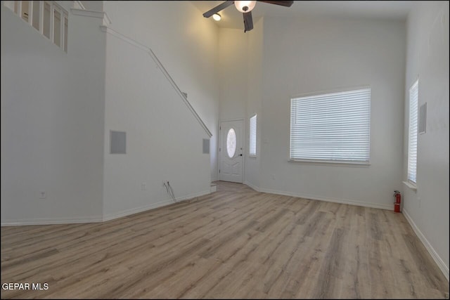 unfurnished living room featuring a high ceiling, ceiling fan, a wealth of natural light, and light wood-type flooring