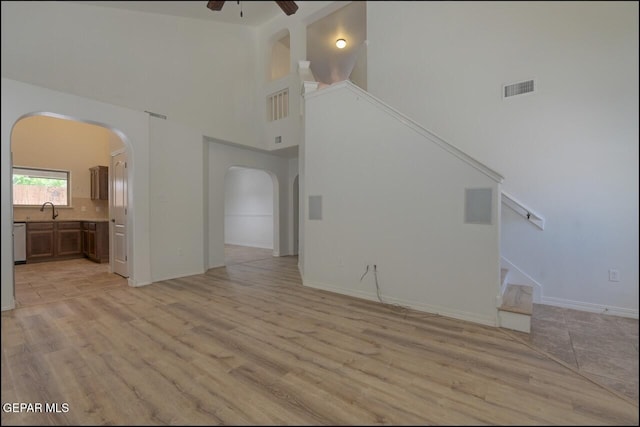unfurnished living room featuring visible vents, a high ceiling, arched walkways, a ceiling fan, and stairs