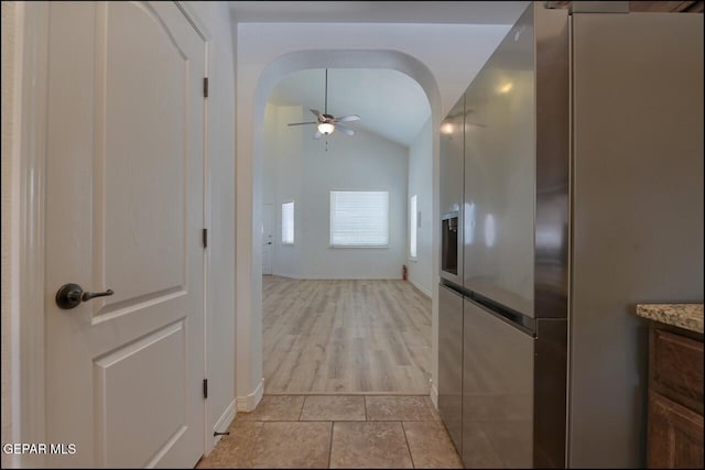 hall featuring arched walkways, lofted ceiling, and baseboards