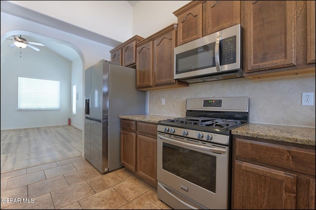 kitchen with light stone counters, stainless steel appliances, ceiling fan, backsplash, and light tile patterned flooring