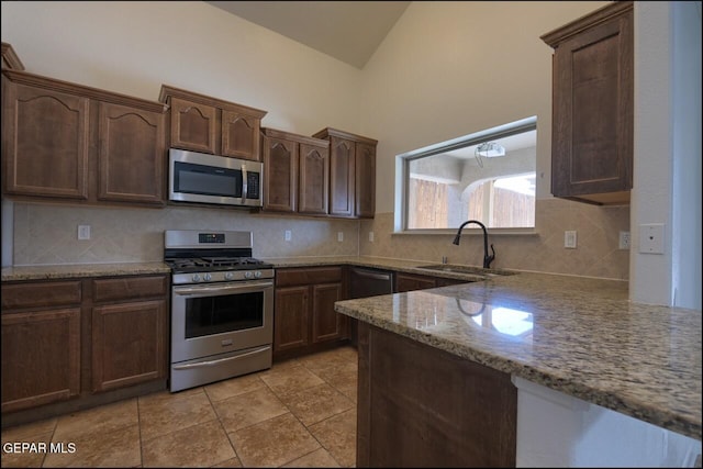kitchen featuring light stone counters, a sink, stainless steel appliances, vaulted ceiling, and backsplash