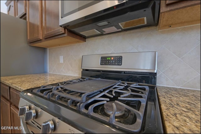 kitchen featuring appliances with stainless steel finishes, brown cabinets, tasteful backsplash, and light stone countertops