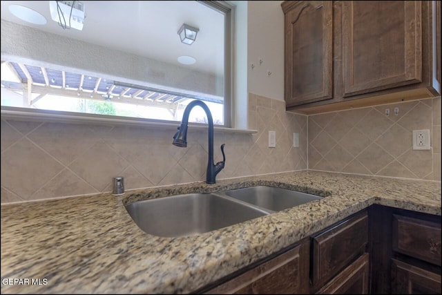 kitchen featuring light stone countertops, backsplash, dark brown cabinetry, and a sink