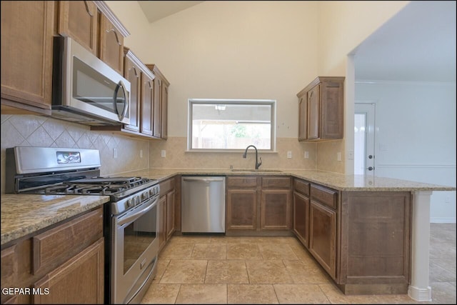 kitchen with tasteful backsplash, light stone counters, stainless steel appliances, a sink, and a peninsula