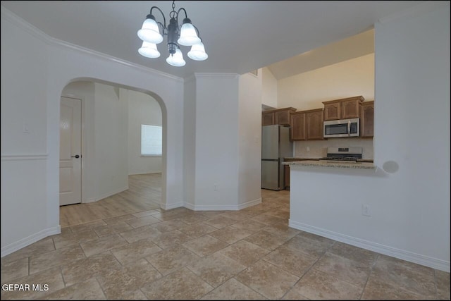 kitchen featuring stone tile flooring, a chandelier, stainless steel appliances, baseboards, and arched walkways