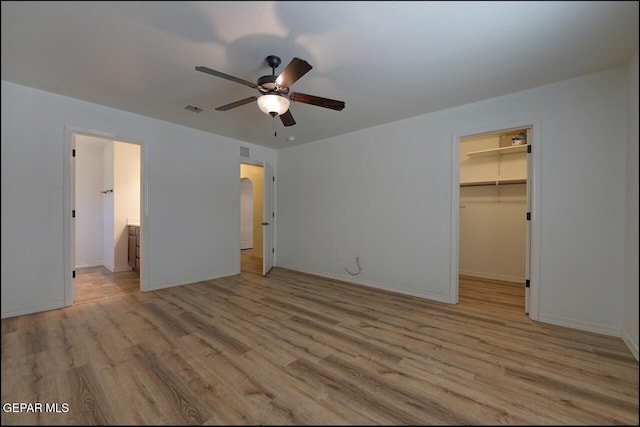 unfurnished bedroom with baseboards, a closet, light wood-type flooring, a walk in closet, and visible vents