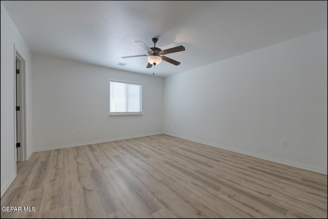 spare room with light wood-style floors, a ceiling fan, visible vents, and baseboards