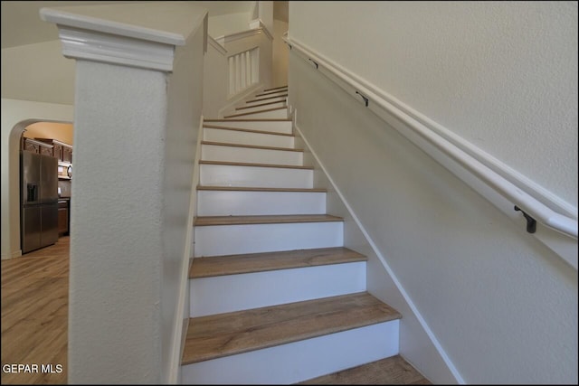 staircase featuring wood finished floors, arched walkways, and a textured wall