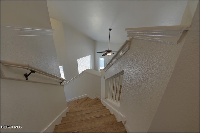 staircase featuring ceiling fan, a textured wall, baseboards, wood finished floors, and high vaulted ceiling