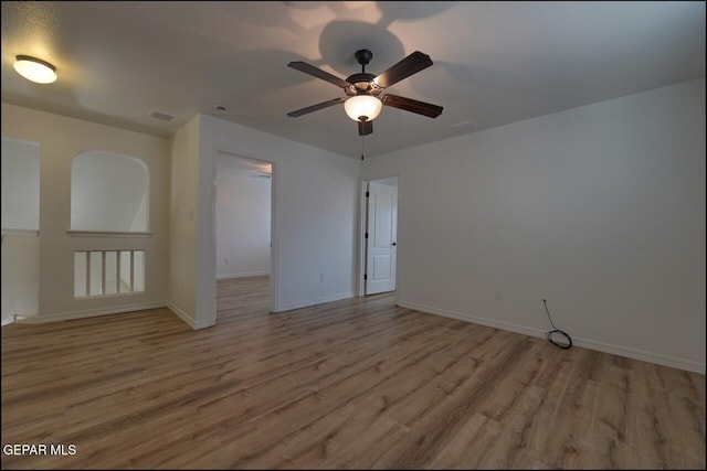 empty room featuring wood finished floors, ceiling fan, visible vents, and baseboards