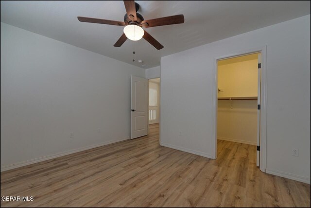 unfurnished bedroom with baseboards, wood finished floors, a closet, ceiling fan, and a walk in closet