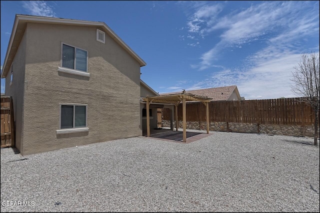 rear view of house with stucco siding, a pergola, a patio, and a fenced backyard