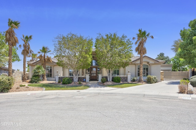 obstructed view of property featuring driveway, stone siding, stucco siding, and fence