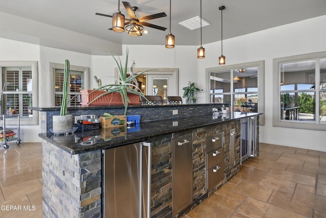 kitchen with dark stone counters, freestanding refrigerator, ceiling fan, a kitchen island, and hanging light fixtures