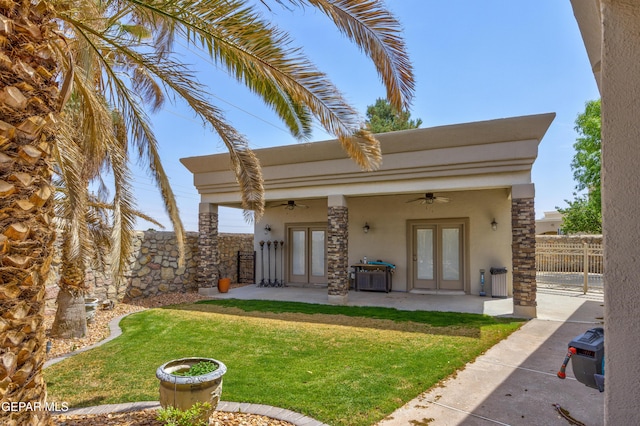 back of property with french doors, fence, a yard, stucco siding, and ceiling fan