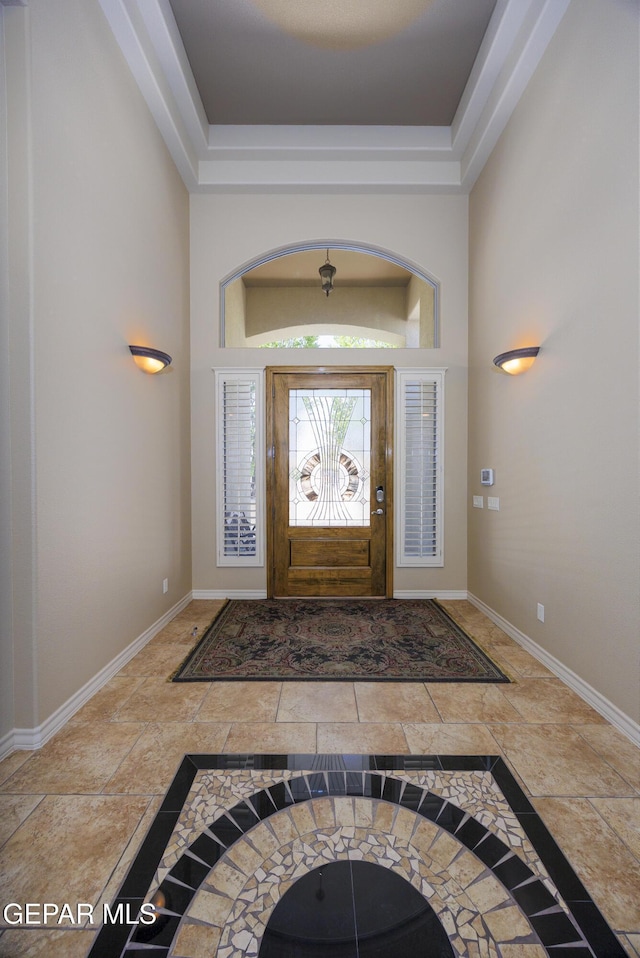 foyer with baseboards, stone tile floors, a high ceiling, and a raised ceiling