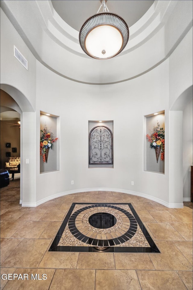 corridor featuring arched walkways, stone tile flooring, visible vents, and baseboards