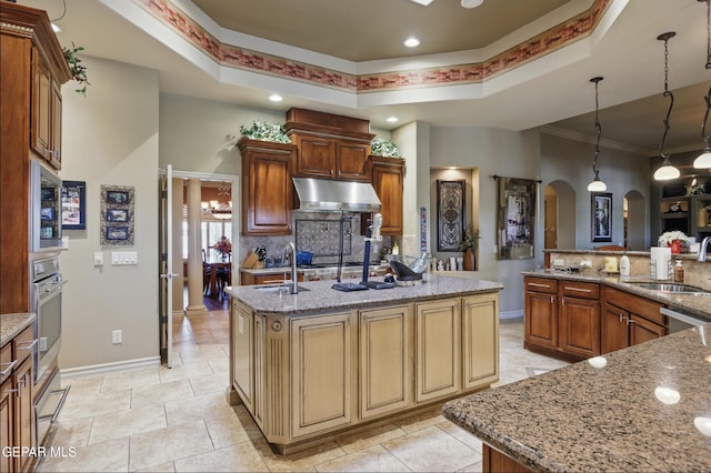 kitchen featuring under cabinet range hood, stainless steel appliances, a sink, arched walkways, and a kitchen island with sink