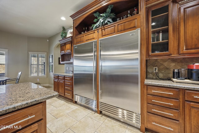 kitchen featuring decorative backsplash, glass insert cabinets, stainless steel built in fridge, light stone countertops, and recessed lighting