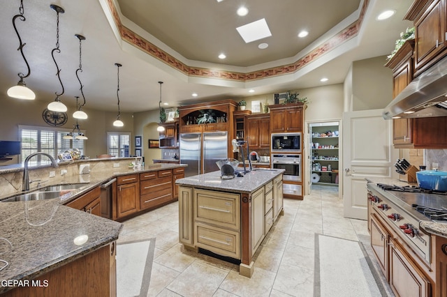 kitchen featuring a sink, a spacious island, a skylight, tasteful backsplash, and built in appliances