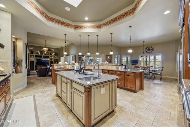 kitchen featuring a large island, a raised ceiling, a sink, light stone countertops, and pendant lighting