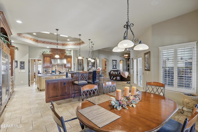 dining space with stone tile floors, a high ceiling, arched walkways, a raised ceiling, and baseboards