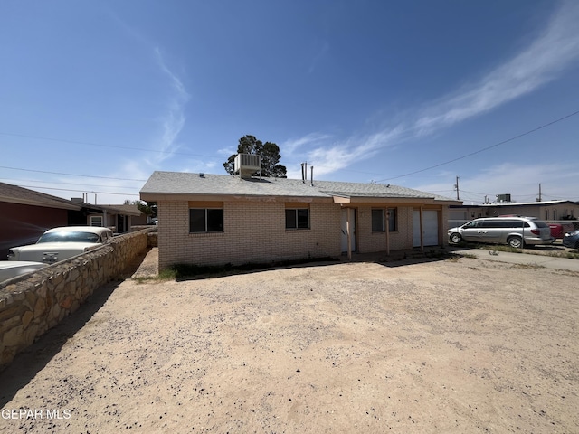 back of property with central AC, brick siding, fence, and a garage